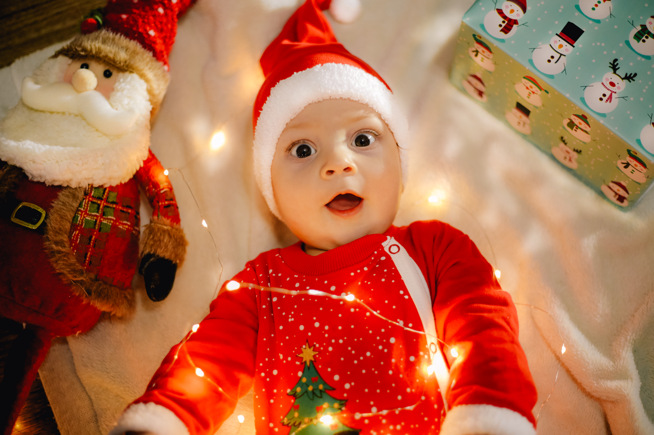 Cute baby in Santa outfit lit by festive Christmas lights.