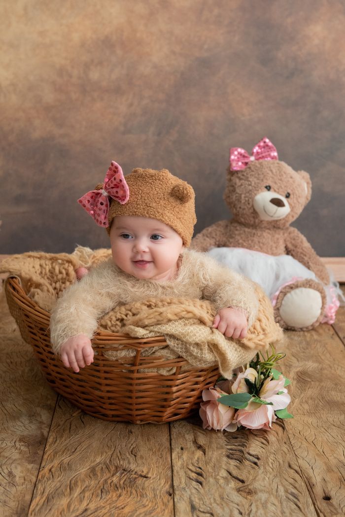 Cute baby girl in a basket with teddy bear in studio setting.